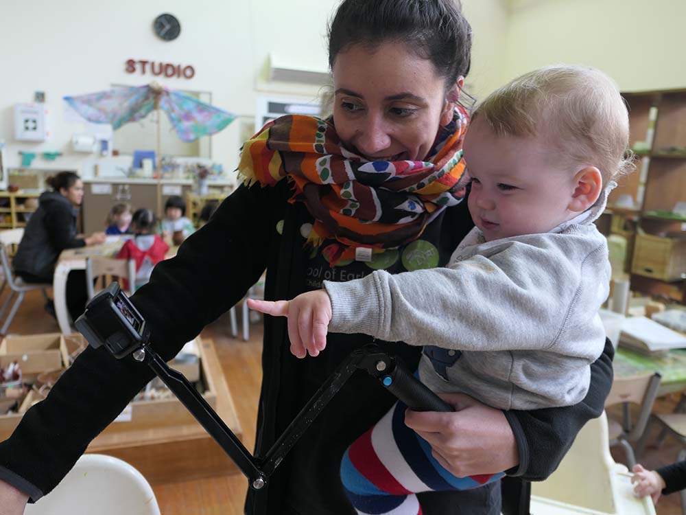 Image of Liz Chavez holding a baby pointing at a GoPro. Liz is our Pedagogical Co-Ordinator.